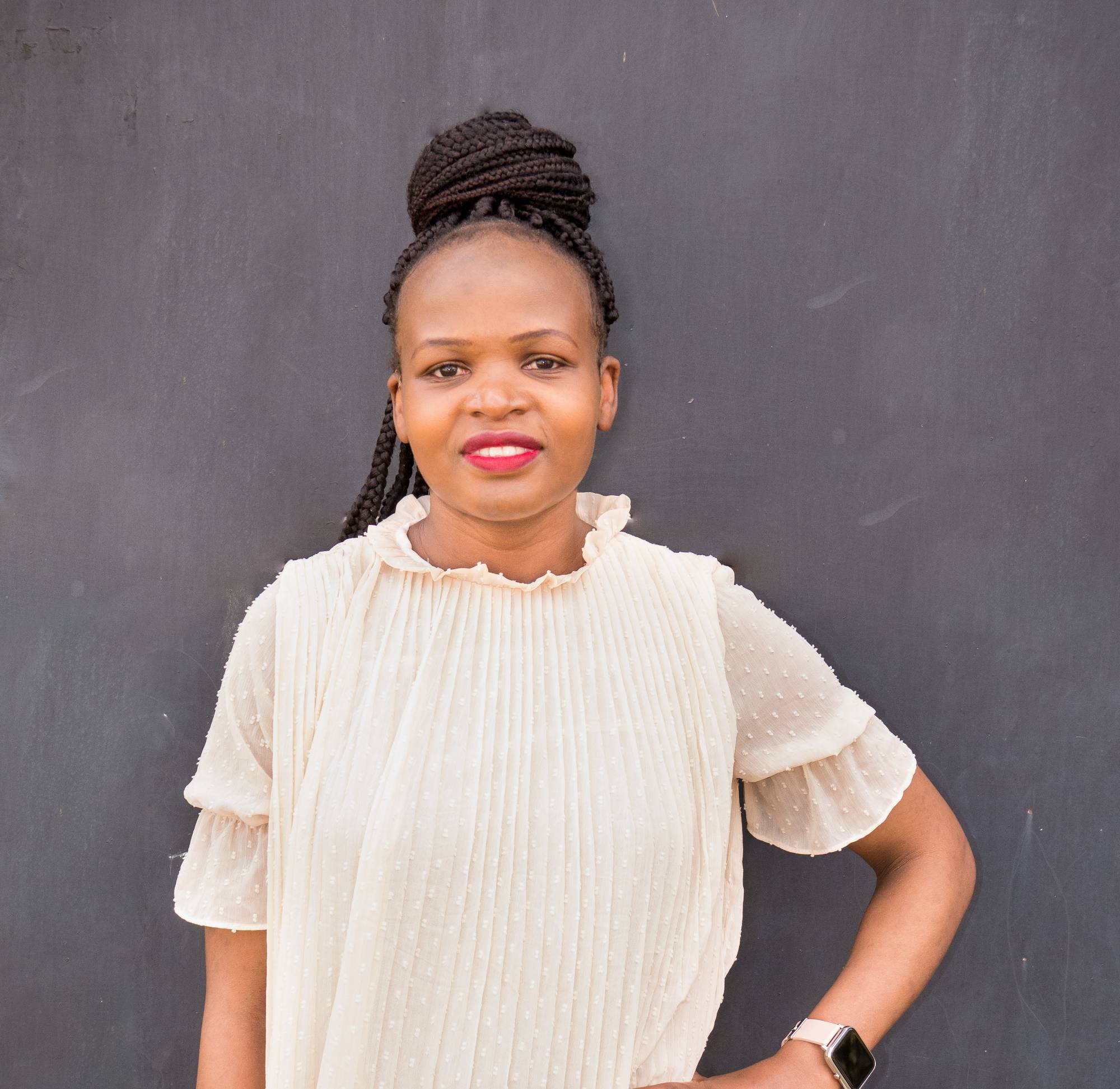 Image of Lynn Obadha standing in front of a gray wall with a white blouse on.